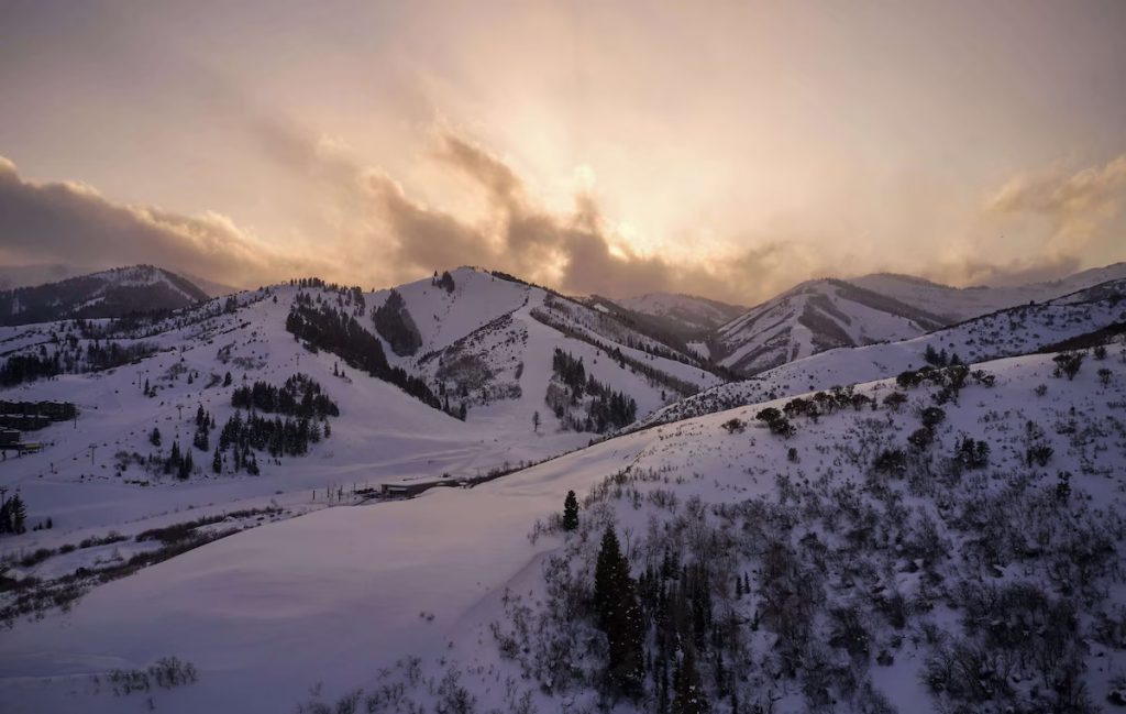 Park City Mountain Resort with snow covered peaks and the cloud covered sun in the background